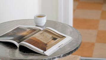 Una mesa redonda con una revista, una taza de café, una silla y un suelo a cuadros.