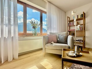 A cozy living room with a sofa, a coffee table, a bookshelf, and a window with a view of mountains. - Bergnest Birkenweg (Pfronten)