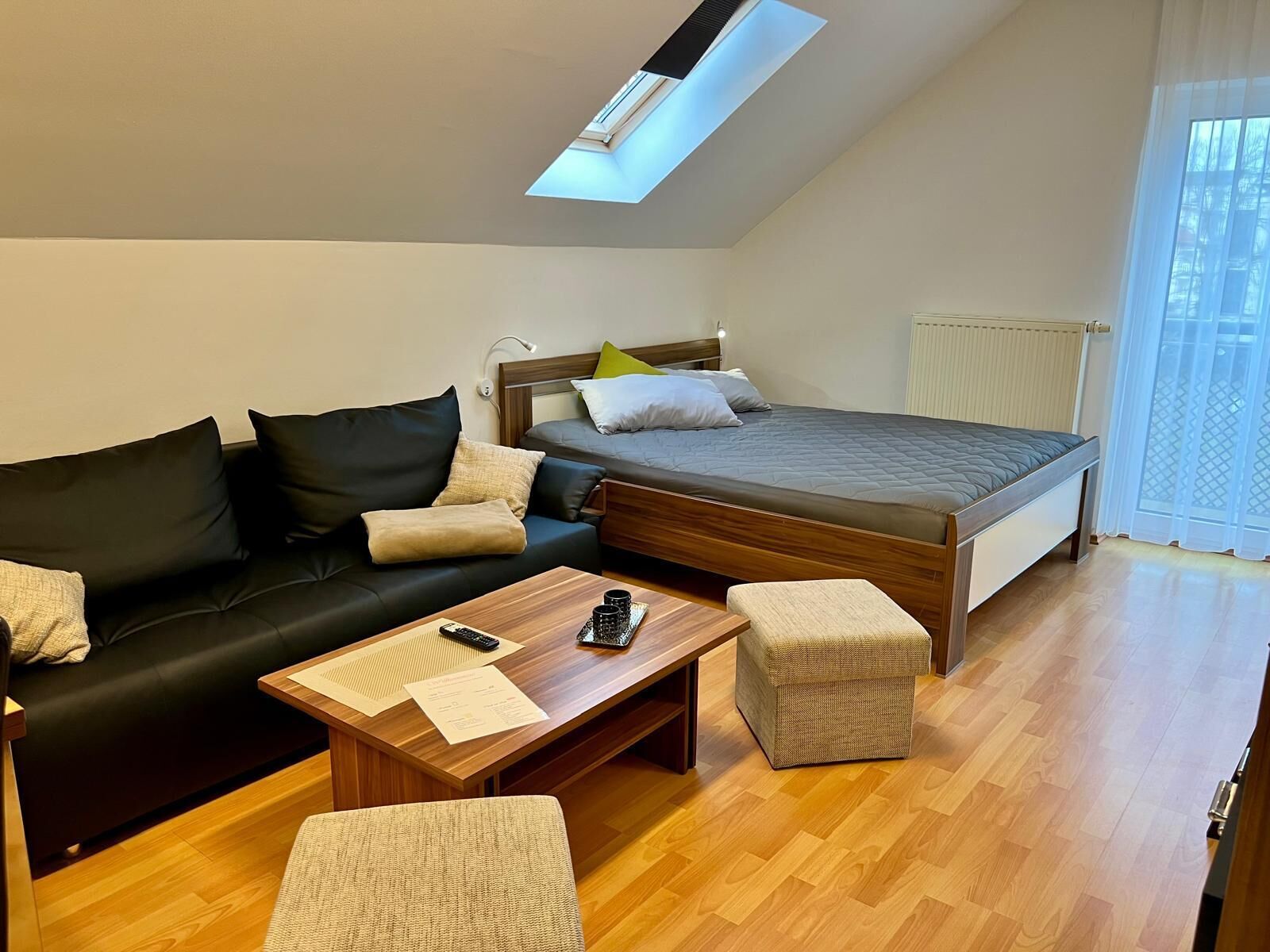 Un dormitorio moderno con cama elevada, una mesa de centro de madera, un sofá y un pequeño reposapiés.