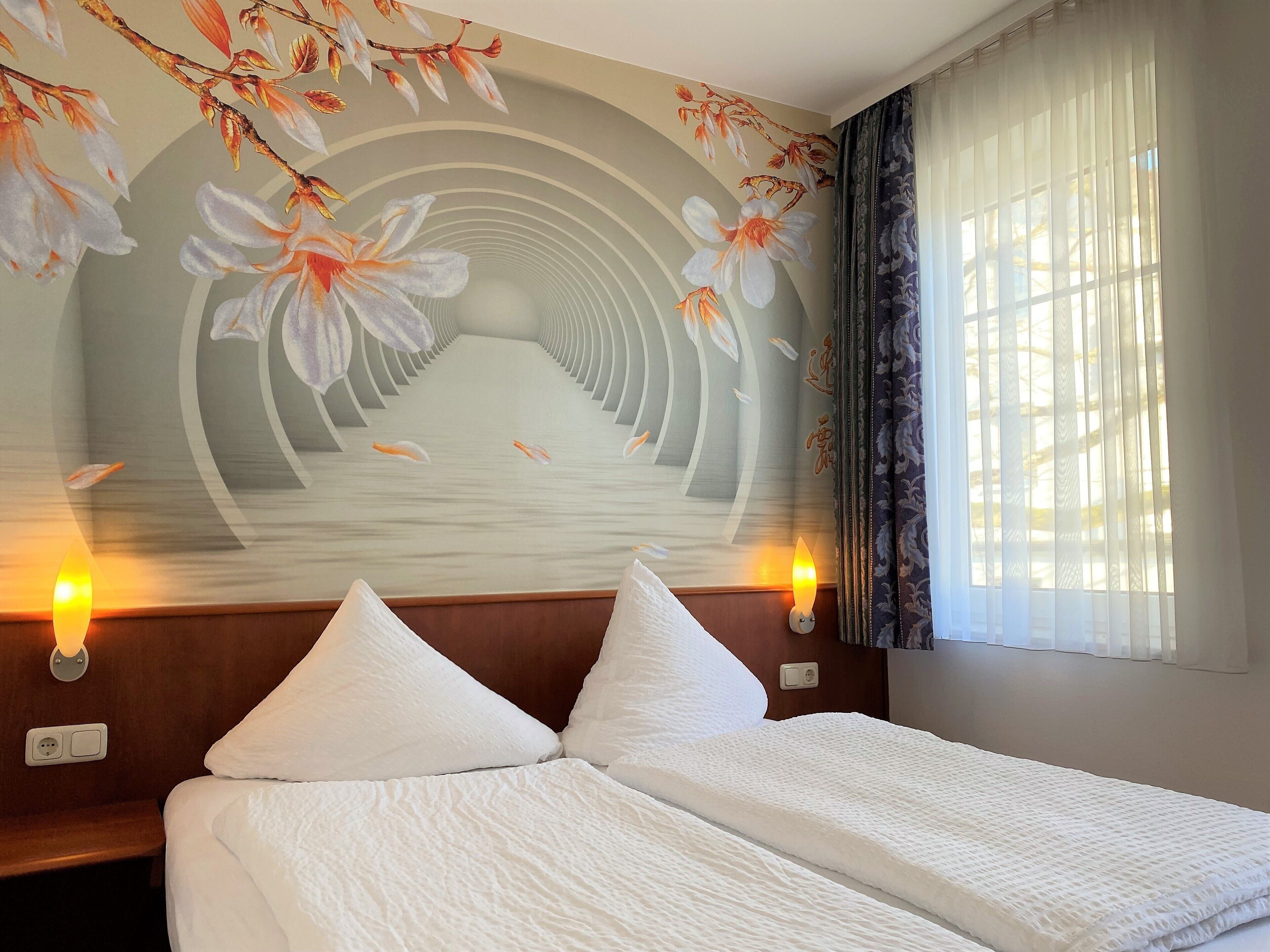 Habitació d'hotel amb dos llits, un mural floral a la paret i dues làmpades penjades a la pared.