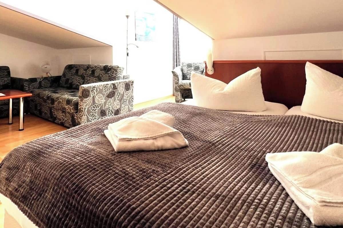 A hotel room with a large bed, two armchairs, a small table, and a window with curtains.