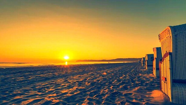 A beach at sunset with a row of beach huts on the right.
