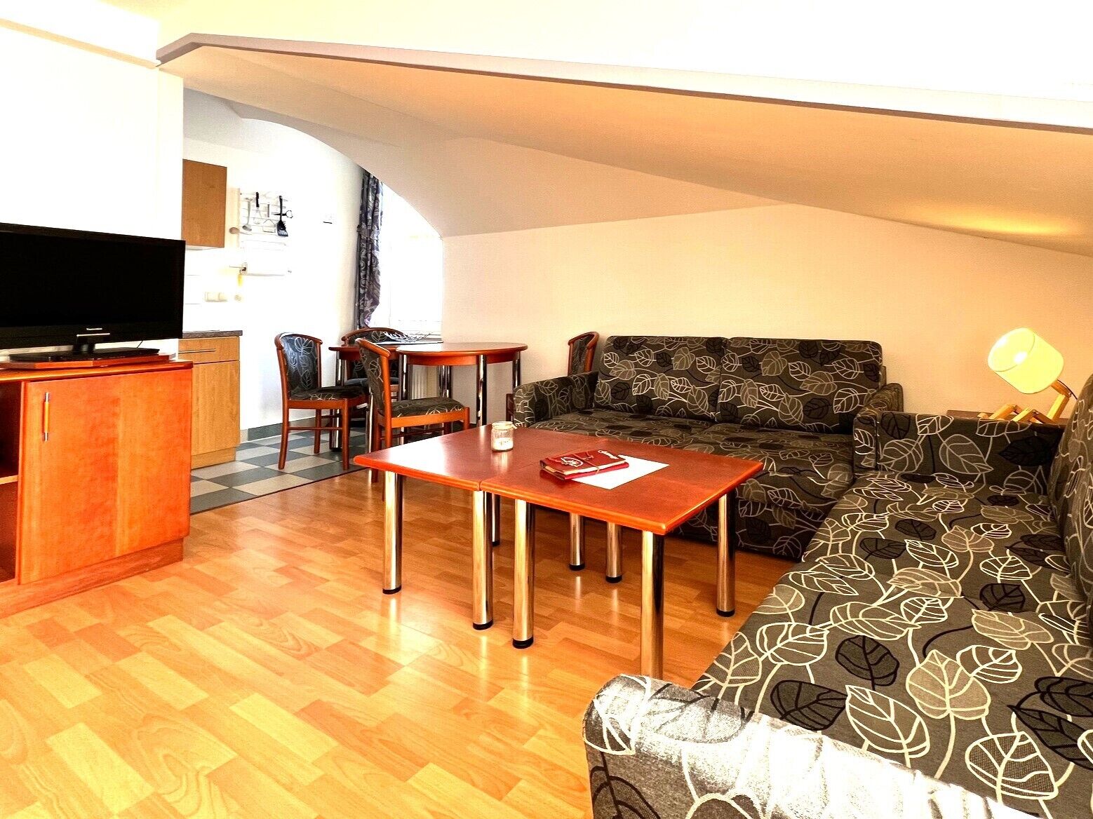 Un ambiente compatto con divano, tavolo da pranzo, televisione e angolo cottura.