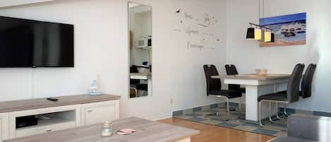 Una sala de estar moderna con un televisor de pantalla plana, una mesa de centro de madera, un sofá, un comedor con sillas y un espejo grande.