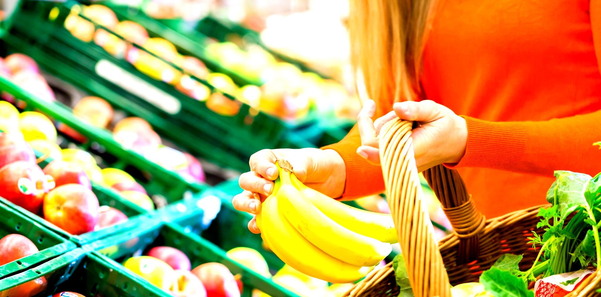 Une personne tenant des bananes et une grappe de pommes dans une épicerie.