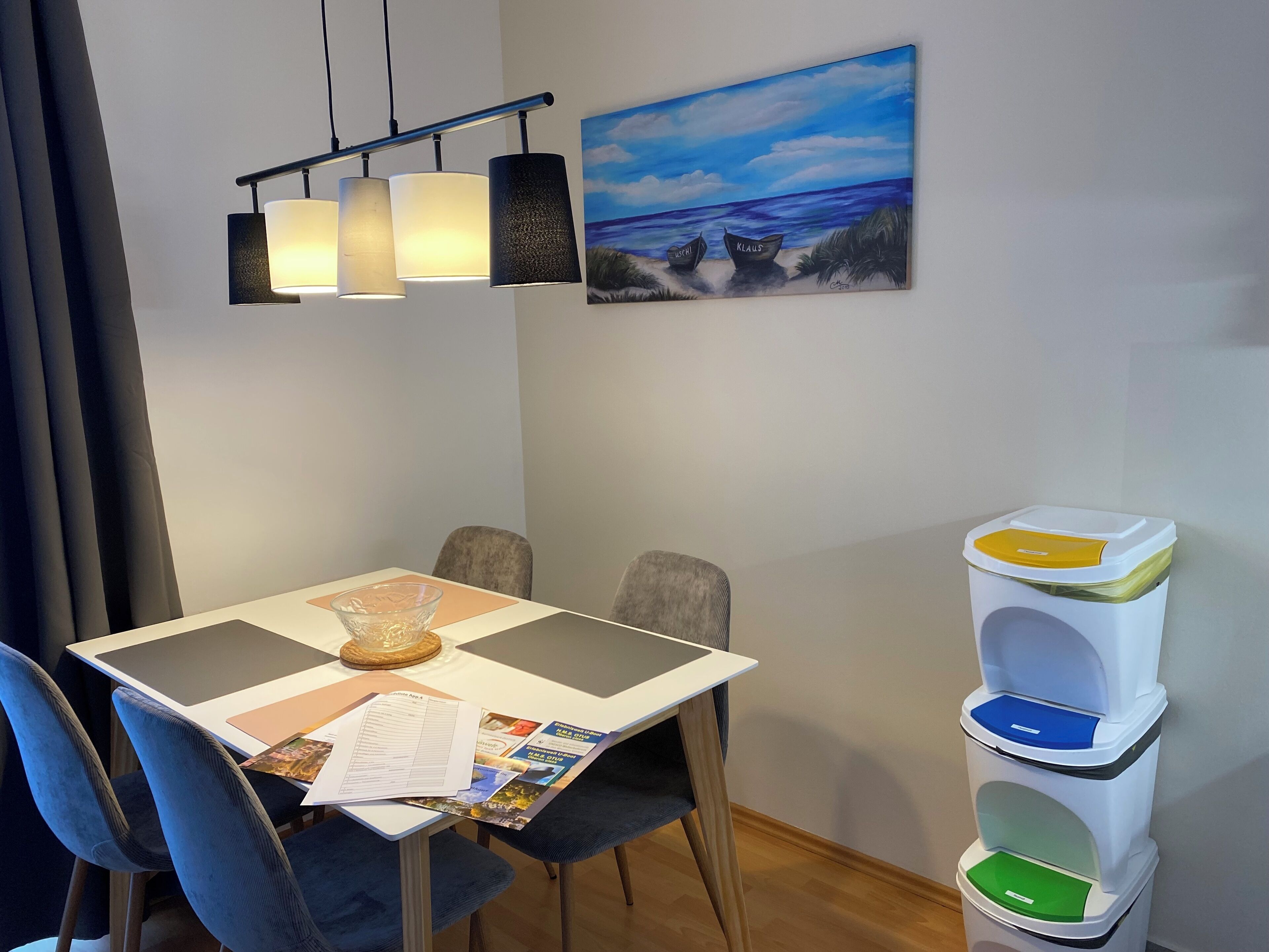 Un espace repas comprenant une table, des chaises, un tableau et une poubelle.
