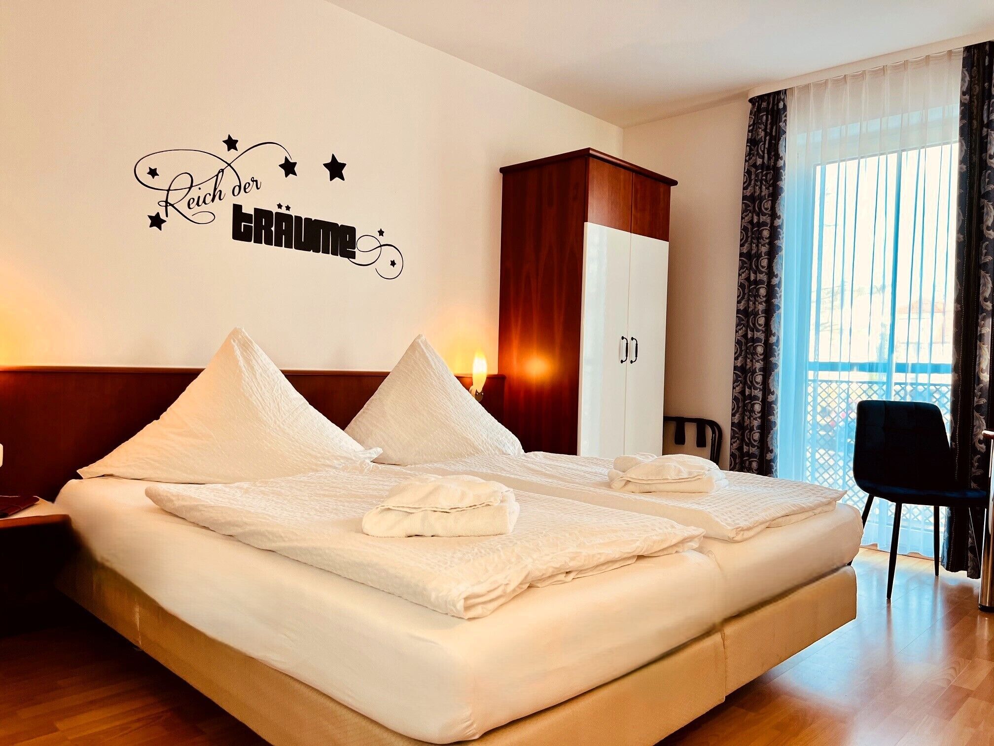 Een hotelkamer met een groot bed, een kledingkast, een bureau en een raam met gordijnen.