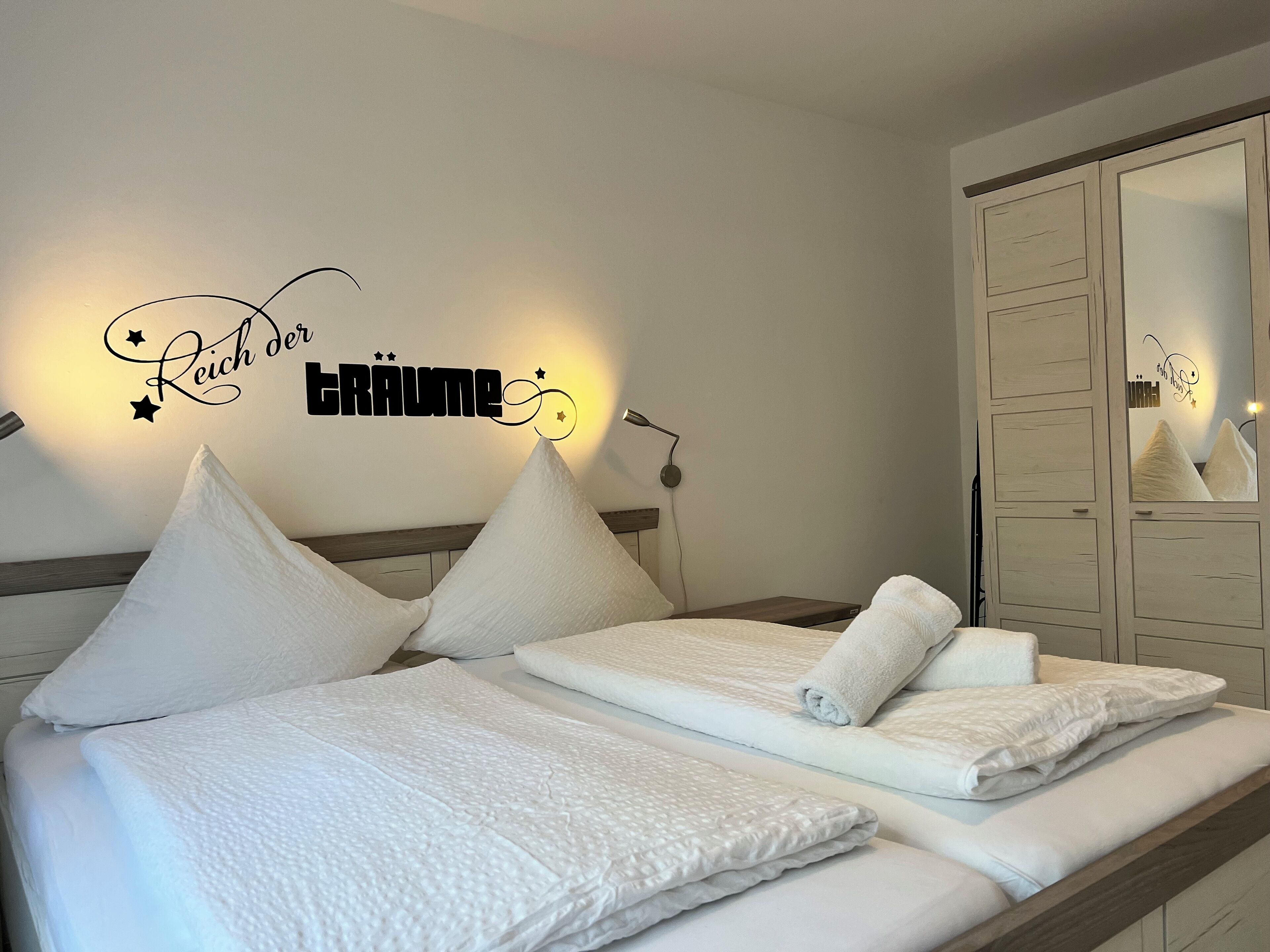 A neatly made bed with white linens and pillows, a bedside lamp, and a wall decoration with text and stars.