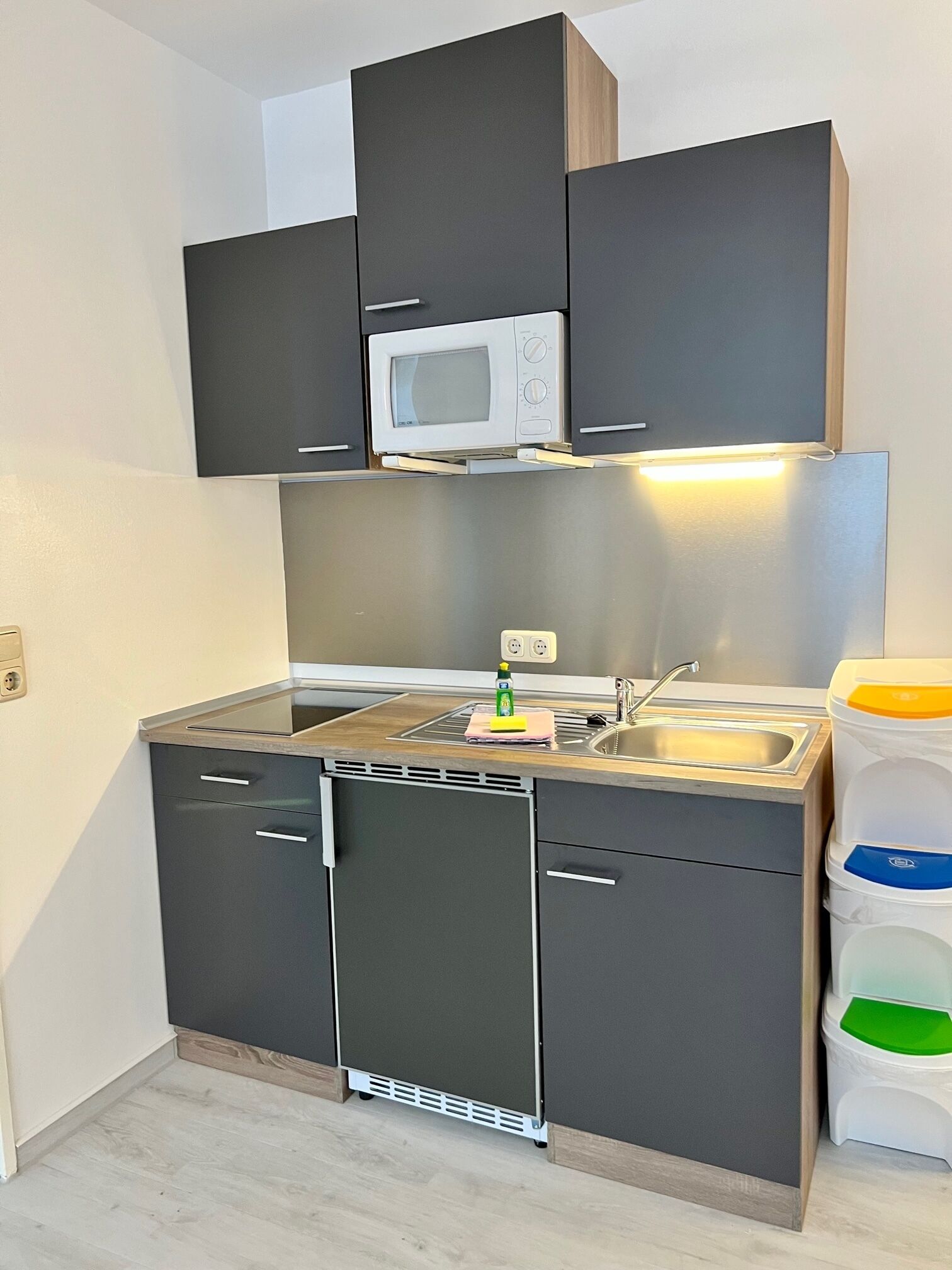 Una cocina pequeña con microondas, lavamanos y armarios.
