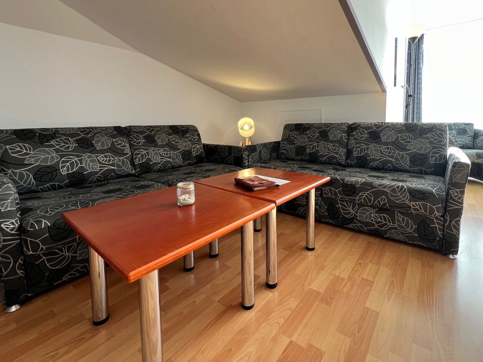 Una sala moderna con una mesa de centro de madera, dos sofás estampados y una lámpara de pie.