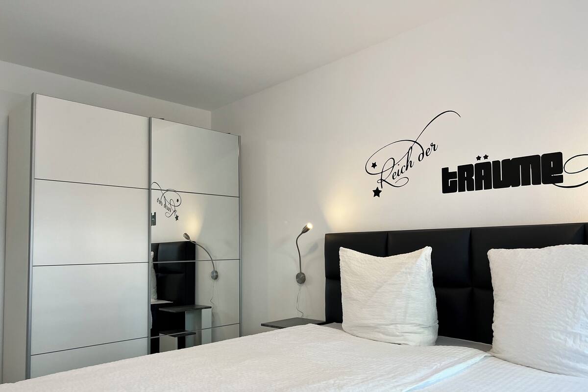 A modern bedroom with a large bed, a black headboard, and a wall-mounted vanity with a mirror.