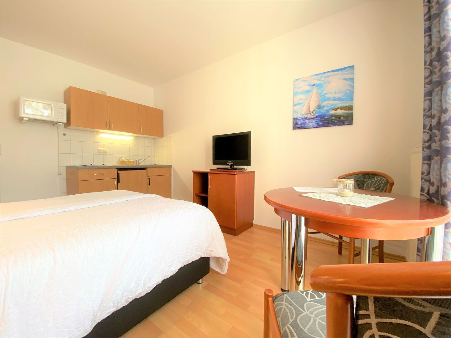 Une chambre d’hôtel comprenant un lit, une petite kitchenette, un téléviseur, une table à manger et un tableau au mur.