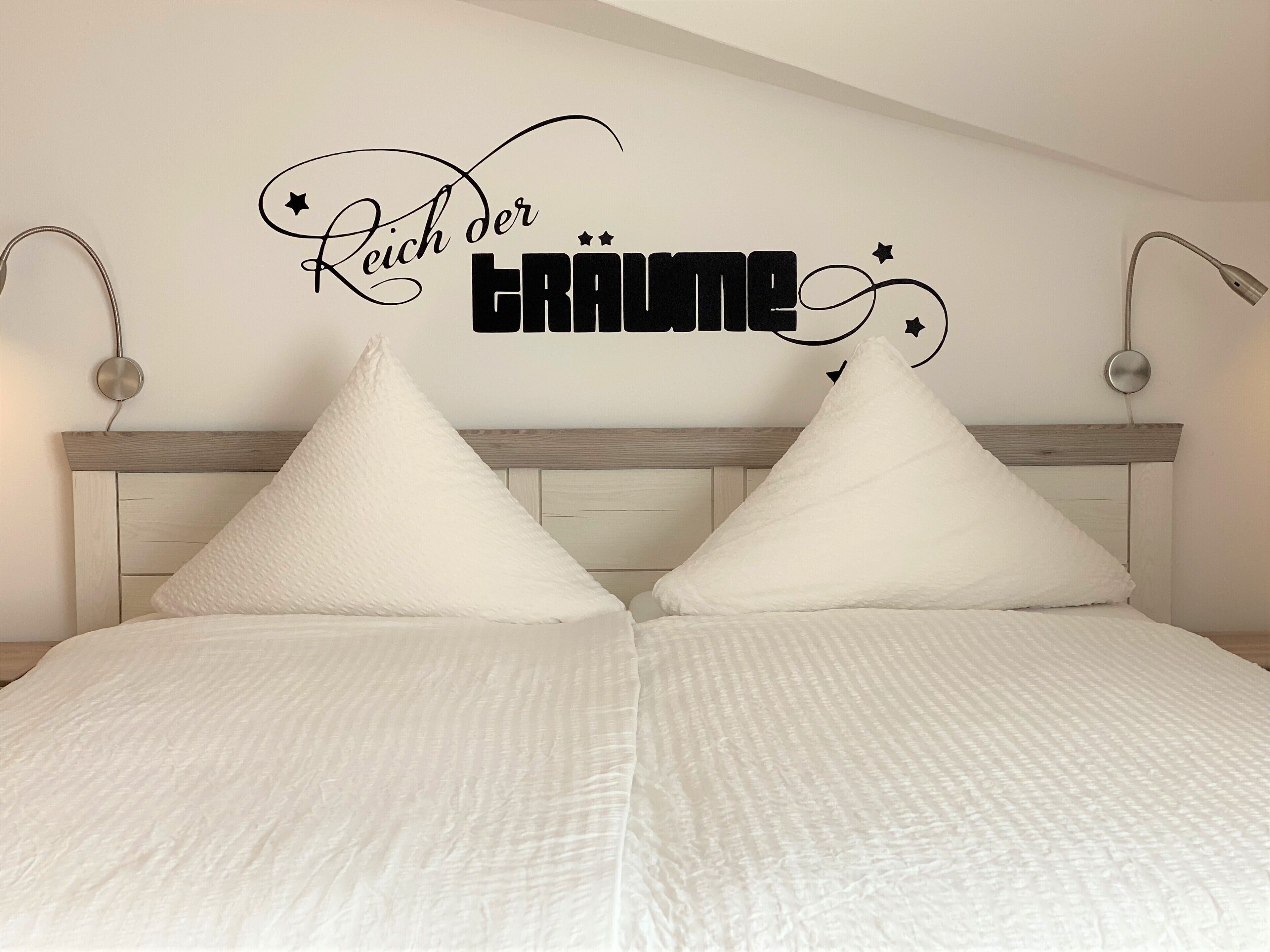 A bedroom with a bed, two pillows, a headboard, and a wall decoration with text.