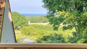 Uma varanda com móveis de vime, uma mesa de metal e vista para uma paisagem verde.