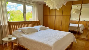 Quarto com cama de madeira, tapete redondo branco, mesa de cabeceira e guarda-roupa.