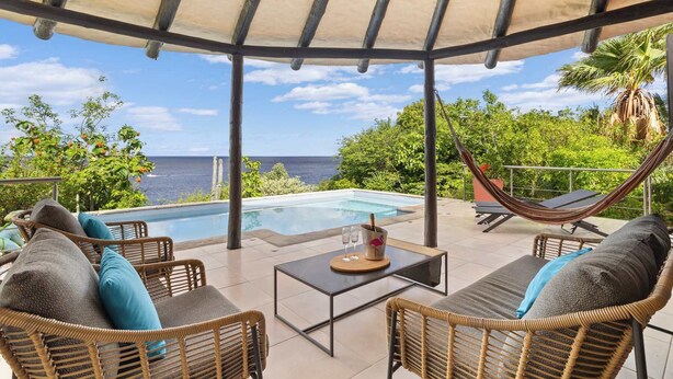 A covered outdoor area with a pool, wicker furniture, and a view of the ocean. - Villa La Brisa with a tropical garden, private pool and spectacular views (Kralendijk)