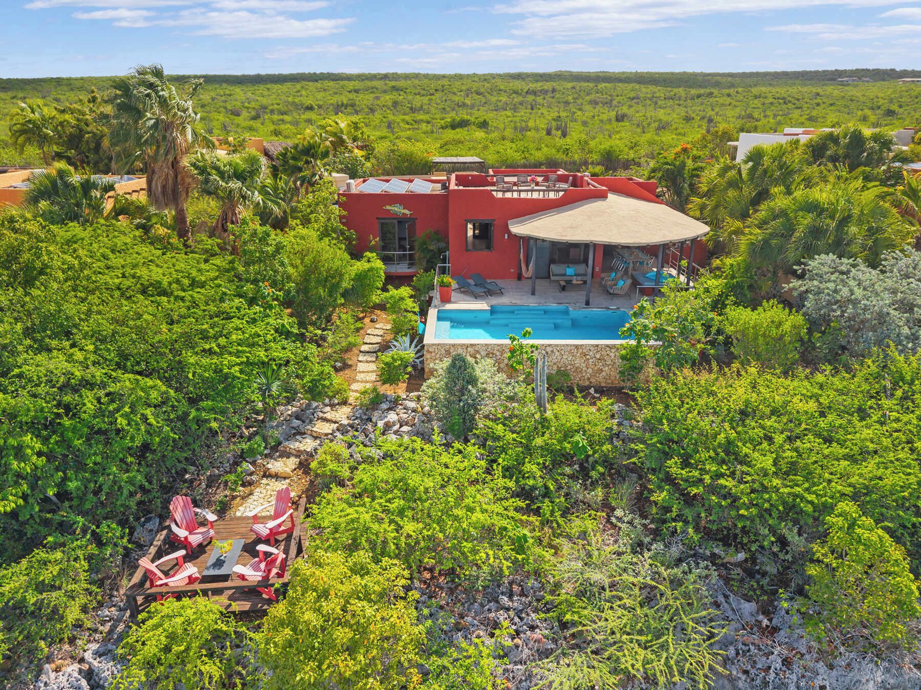 Una villa roja con piscina rodeada de exuberante vegetación.