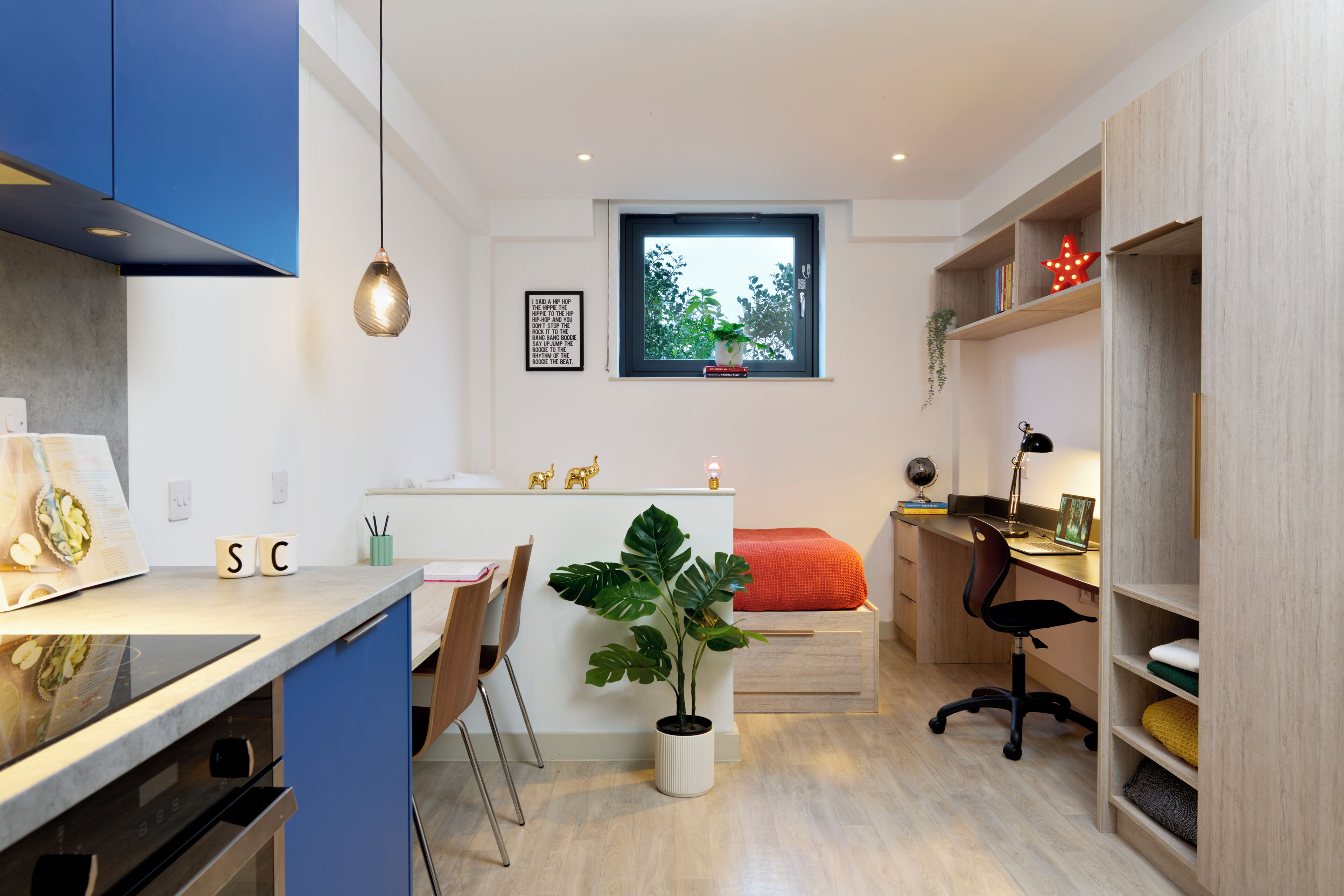 A compact, modern room with a kitchenette, a dining area, and a workspace.