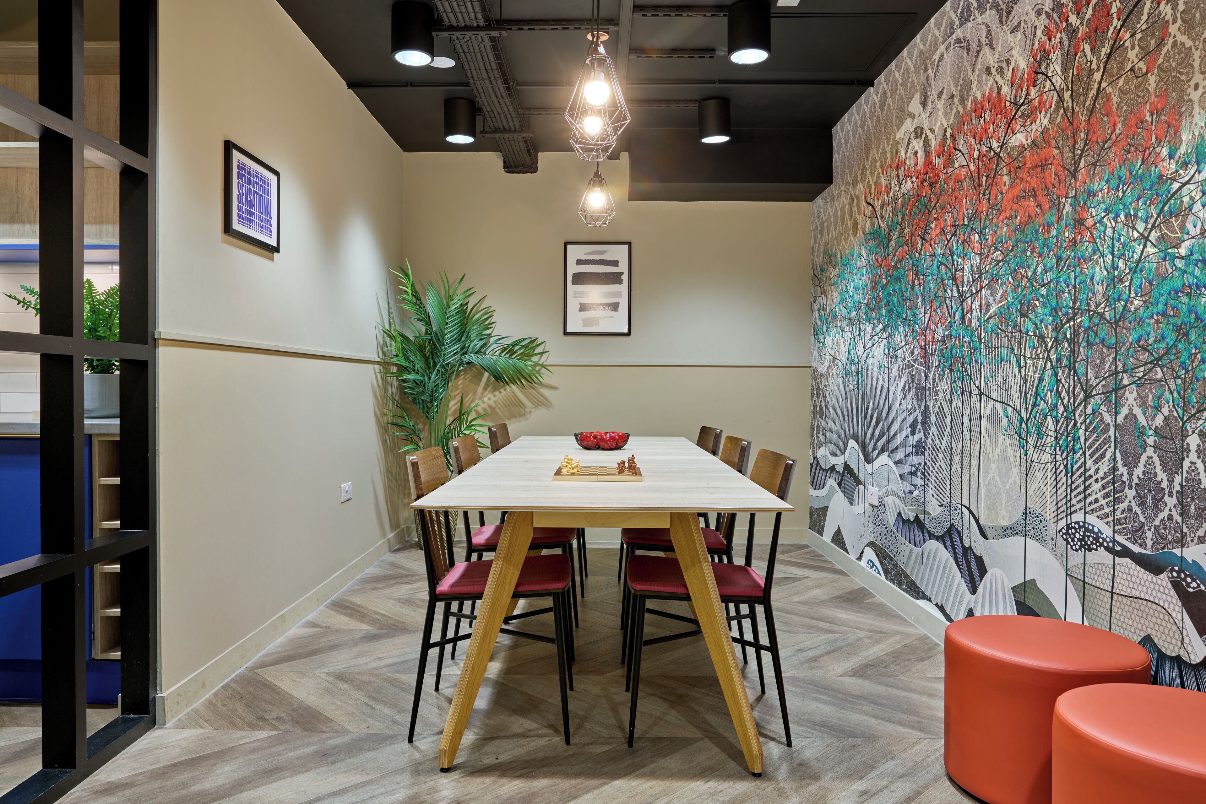 A dining area with a white table, red chairs, and a colorful mural on the wall.