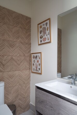 Een badkamer met een visgraatmozaïek wand, een witte wastafel, een spiegel en twee ingelijste botanische prints.