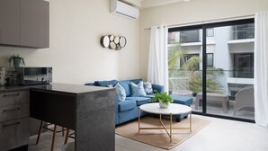 A modern living room with a grey sofa, a round coffee table, and a large sliding glass door to an outdoor balcony. - Cozy 1BR in Panorama Lake • Pool & Beach (PUNTA CANA)