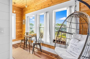 A room with a wooden ceiling, a hanging chair, a table with chairs, and large windows.