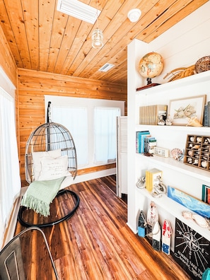 A cozy room with wooden walls and ceiling, a hanging chair, a bookshelf with books and decorative items, and a globe on the wall.