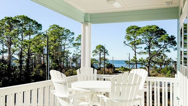 A covered outdoor area with a wooden deck, white chairs, and a table.