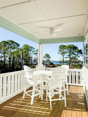 A covered outdoor area with a wooden deck, white chairs, and a table.