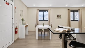 Een moderne hotelkamer met een zithoek, een witte deur met nooduitgangsborden, een brandblusser en een raam met uitzicht op besneeuwde bomen.