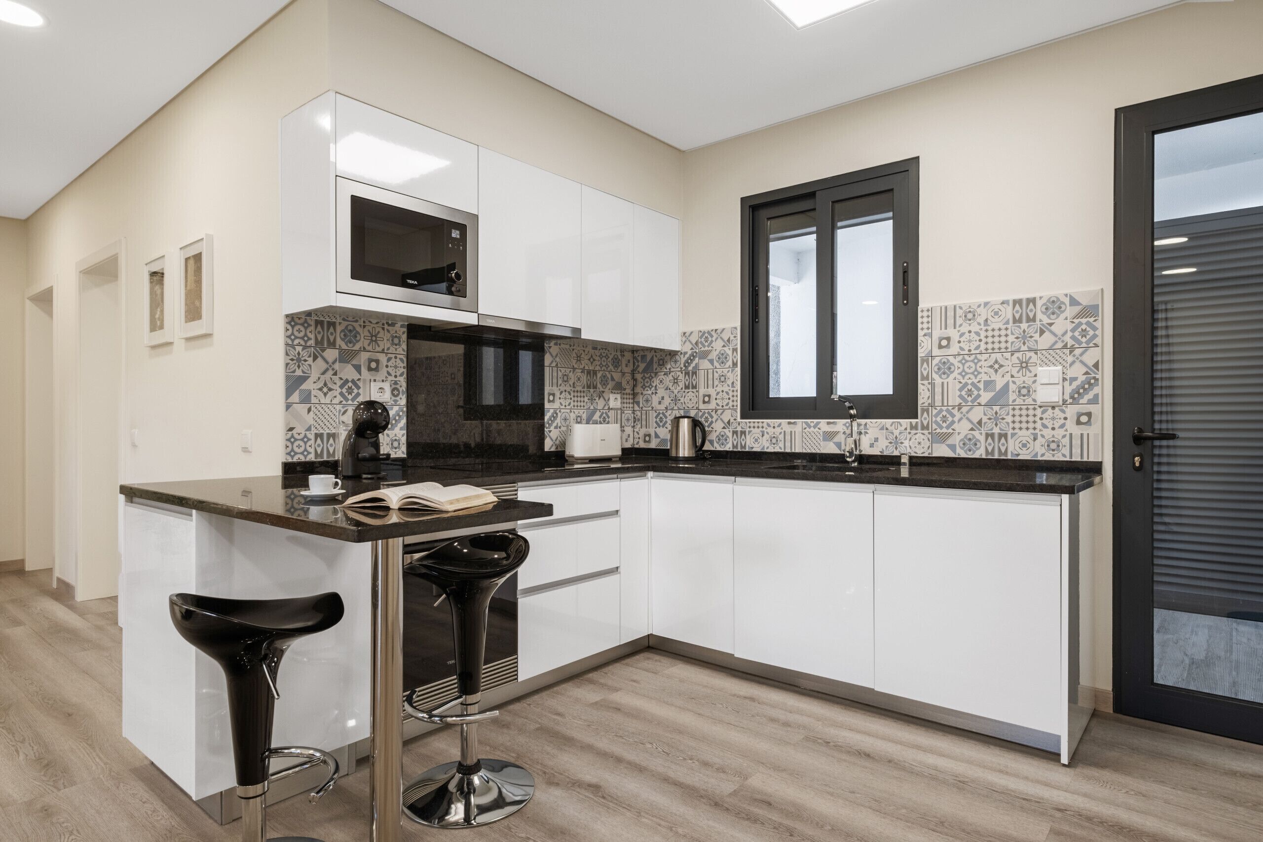 A modern kitchen with white cabinets, a black countertop, and a patterned backsplash.
