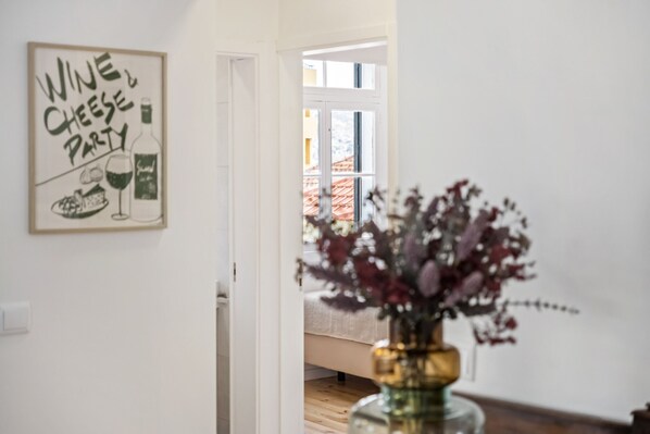 Una habitación con un cartel enmarcado en la pared, suelo de madera y un jarrón con flores sobre una mesa.