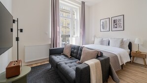 Una camera d'albergo moderna con un letto grande, un divano grigio, un tavolino e una televisione.