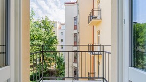 Un balcon doté d’une balustrade en métal, donnant sur un quartier résidentiel avec des arbres et des immeubles à plusieurs étages.