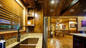Ein Holzinterieur mit Küchenbereich, der eine Arbeitsplatte aus Granit, ein Spülbecken und eine Billardkugelbahn zeigt. Außerdem ist Holzboden verlegt.