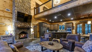 A spacious living area with a stone fireplace, leather sofas, and a kitchen with a bar.