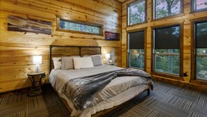 A wooden cabin bedroom with a bed, two bedside tables, and large windows.