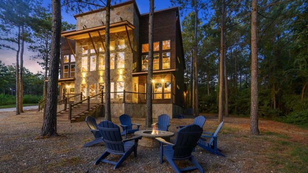 A lodge with a stone exterior, a wooden deck, and a fire pit surrounded by Adirondack chairs.