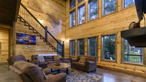 A spacious living room with a fireplace, large windows, and a staircase leading to upper floors.
