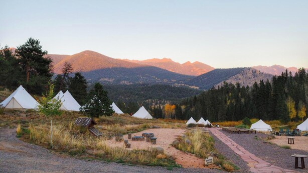 Un camping con varias tiendas de campaña, un sendero de grava y montañas al fondo.