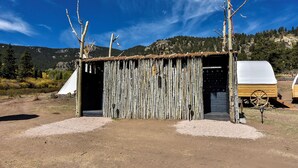Una estructura rústica de madera con techo de paja, un carretón de madera y suelo de tierra.