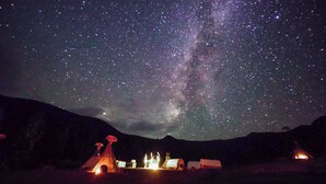 Cielo estrellado con la Vía Láctea visible, una fogata y un tipi.
