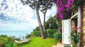 Une maison en pierre avec une cour verdoyante, un banc et une vue sur la mer.