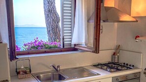 Une cuisine compacte avec une fenêtre donnant sur la mer, un évier, une cuisinière et un réfrigérateur.