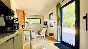 Una cocina moderna con comedor, armarios de madera, encimera negra y un amplio ventanal corredero que da a una terraza exterior.