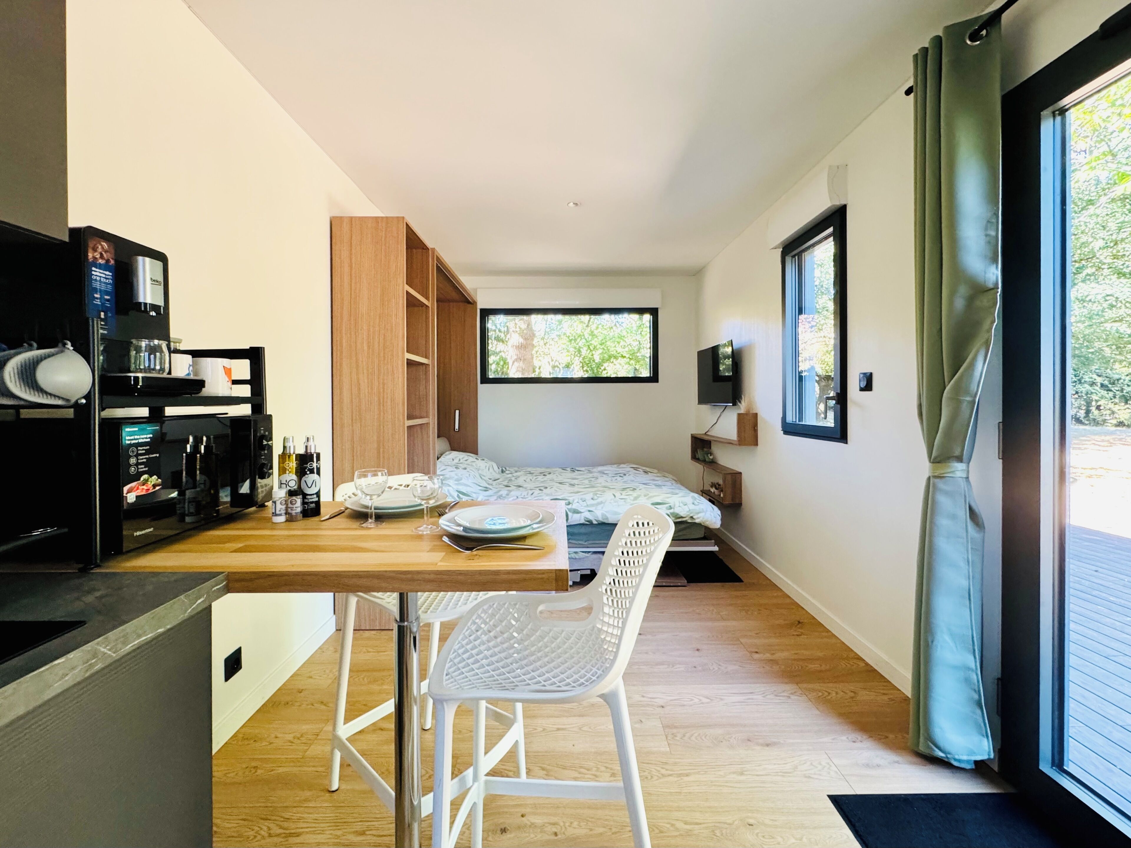 A compact bedroom with a bed, a small desk with a chair, a TV, and a window with curtains.