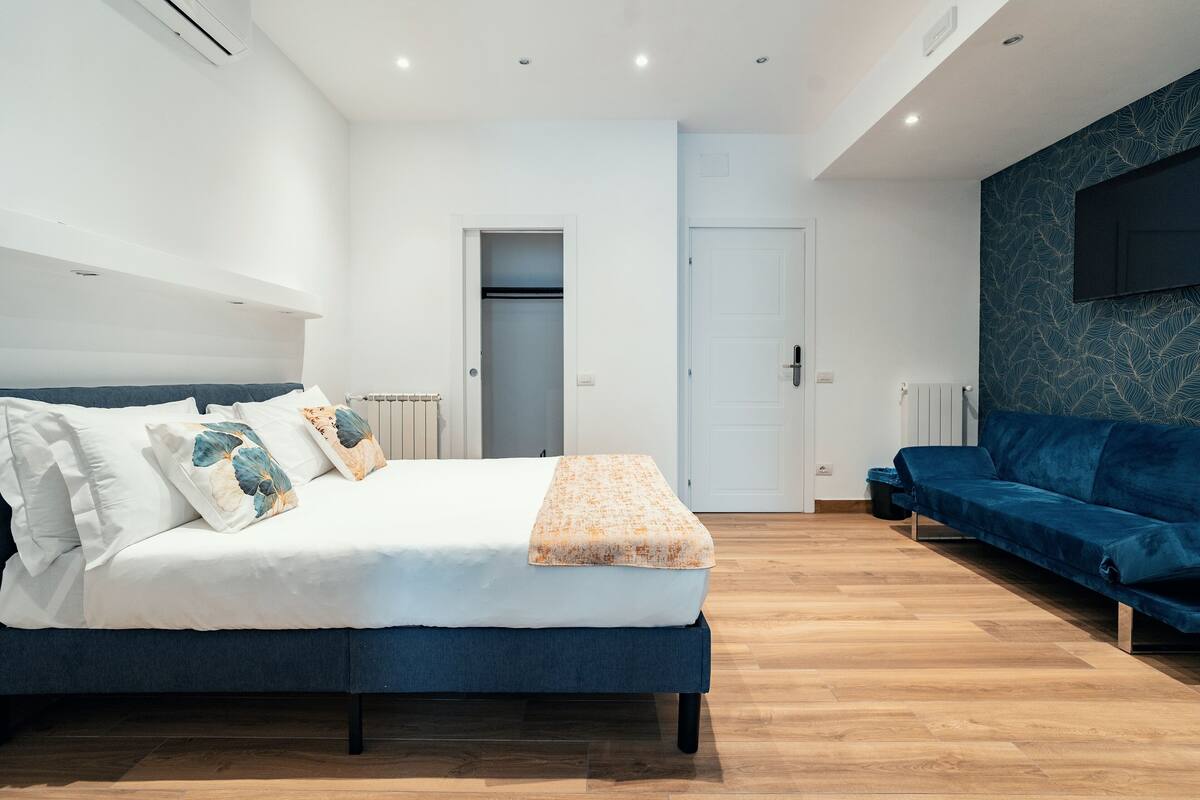 Un dormitorio moderno con cama, sofá azul y televisor montado en la pared.