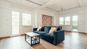 A spacious living room with a dark blue sofa, a wooden coffee table, and large windows. - Casa Mia SanPietro (Rome)