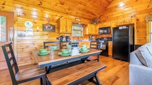A wooden cabin interior with a dining table set for four, a kitchen with modern appliances, and a cozy seating area. - Amazing 2BD Cabin w/ VIEWS! Hot Tub (Sevierville)