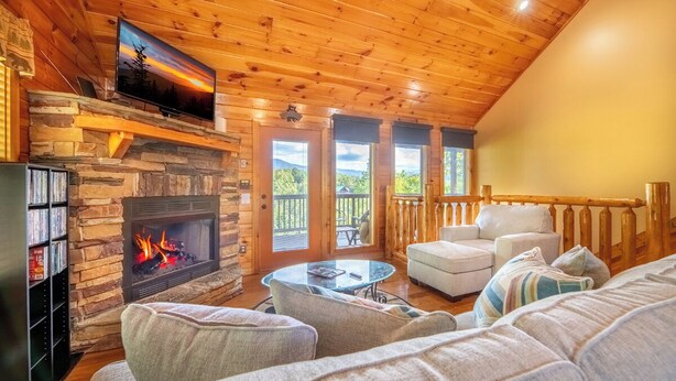 A cozy cabin interior with a stone fireplace, wooden ceiling, and a balcony with a railing. - Amazing 2BD Cabin w/ VIEWS! Hot Tub (Sevierville)